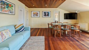 A living room with a wooden ceiling, a light blue sofa, a dining table with chairs, and framed pictures on the walls. - Setúbal Downtown Nº97B (Setúbal)