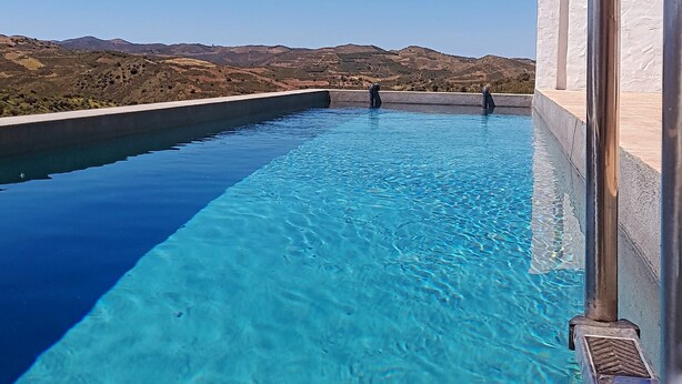 Una piscina a sfioro blu cristallina con vista su dolci colline lontane.