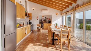 Cucina con mobili in legno, frigorifero in acciaio inossidabile, tavolo con sedie e vista panoramica tramite ampie porte scorrevoli in vetro.