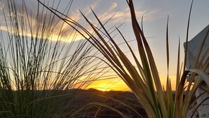 Een zonsondergang boven hoog gras en rotsen.