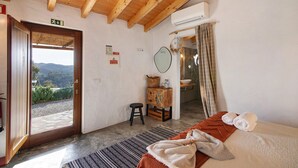 Een kamer met een houten plafond, een bed met dekbed, een klein krukje, een houten kast, een spiegel en een airconditioning.