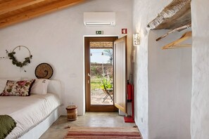 Un dormitorio con cama, aire acondicionado de pared, una puerta que da al exterior y un taburete de madera.