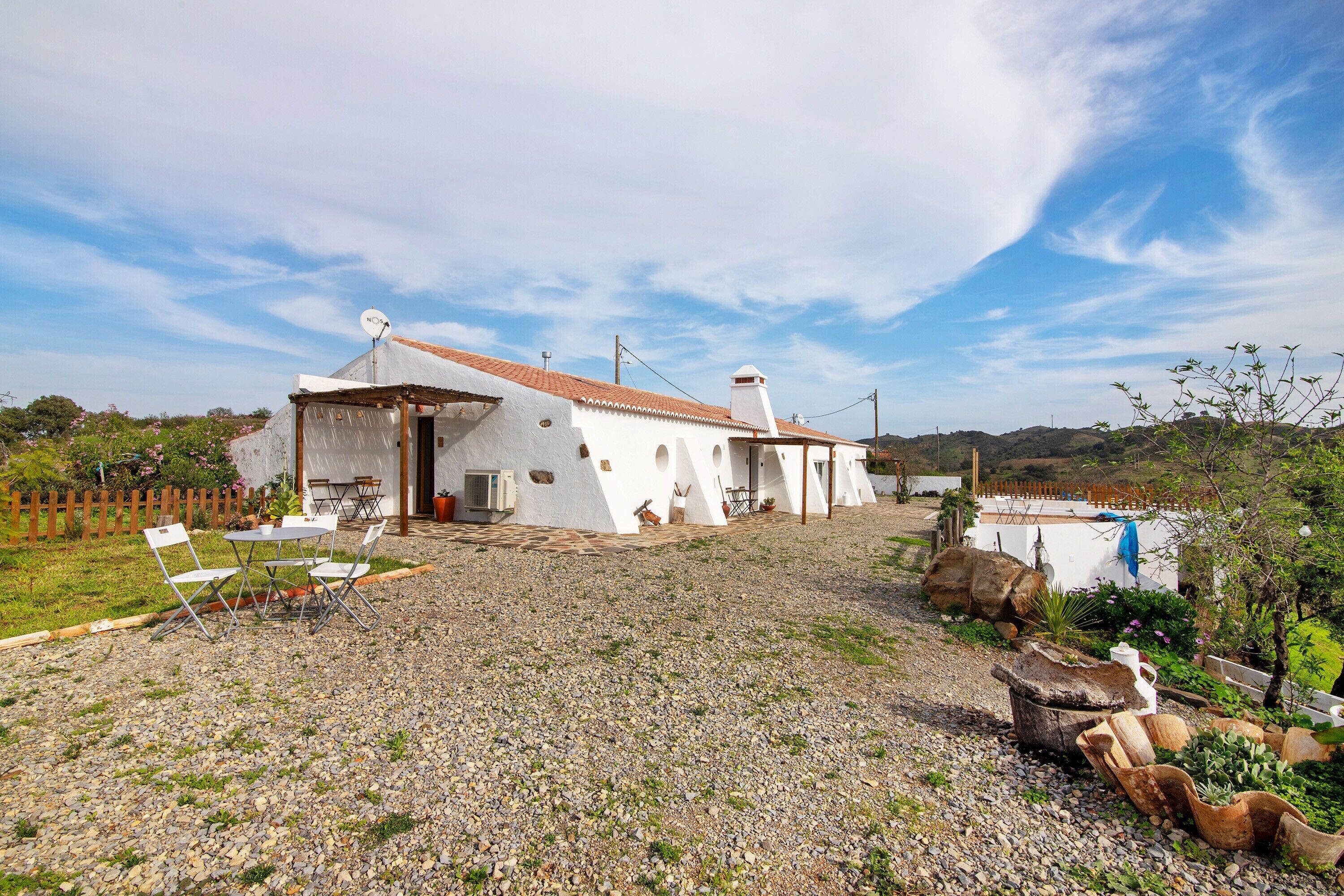 Una casa blanca con camino de grava, mobiliario exterior y piscina.