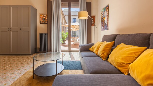 A living room with a sofa, a glass table, a radiator, and a view through a glass door.