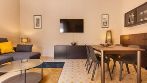 A modern living room with a sofa, coffee table, TV, and dining area.