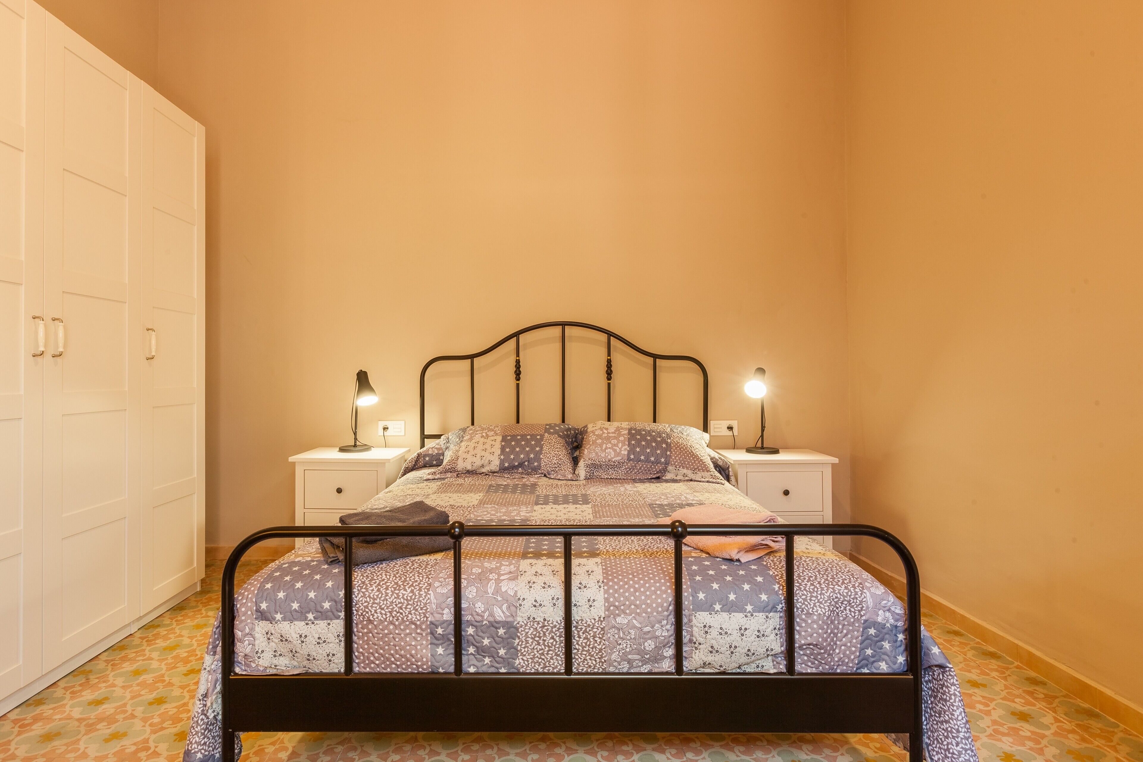 Um quarto com uma cama, mesas de cabeceira e um guarda-roupa.
