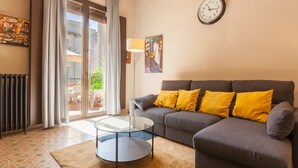 A living room with a sofa, a glass coffee table, a radiator, a clock, and a painting on the wall.