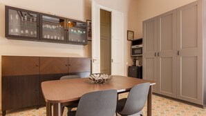 A dining area with a wooden table, two chairs, a decorative bowl, a cabinet with glassware, and a wardrobe.