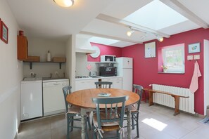 A compact kitchen with white appliances, a wooden dining table, and chairs. - Holiday Home 'La Maison De Pêcheur Chez Alice' with Private Terrace, Private Garden and Wi-Fi (Pontrieux)