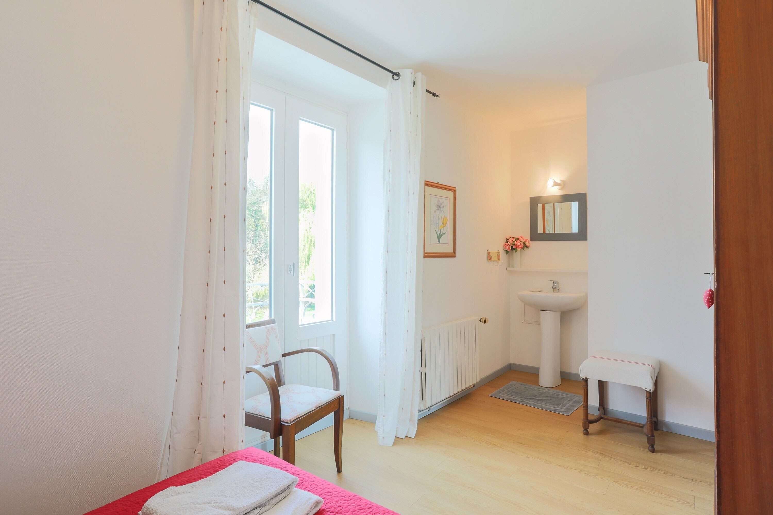 A room with a bed, a chair, a small table, a sink, and a window with curtains.