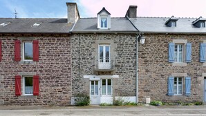 A stone building with red shutters, a small balcony, and a door.