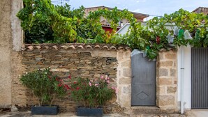 Un muro de piedra con una puerta, plantas en macetas y un balcón cubierto de hiedra.