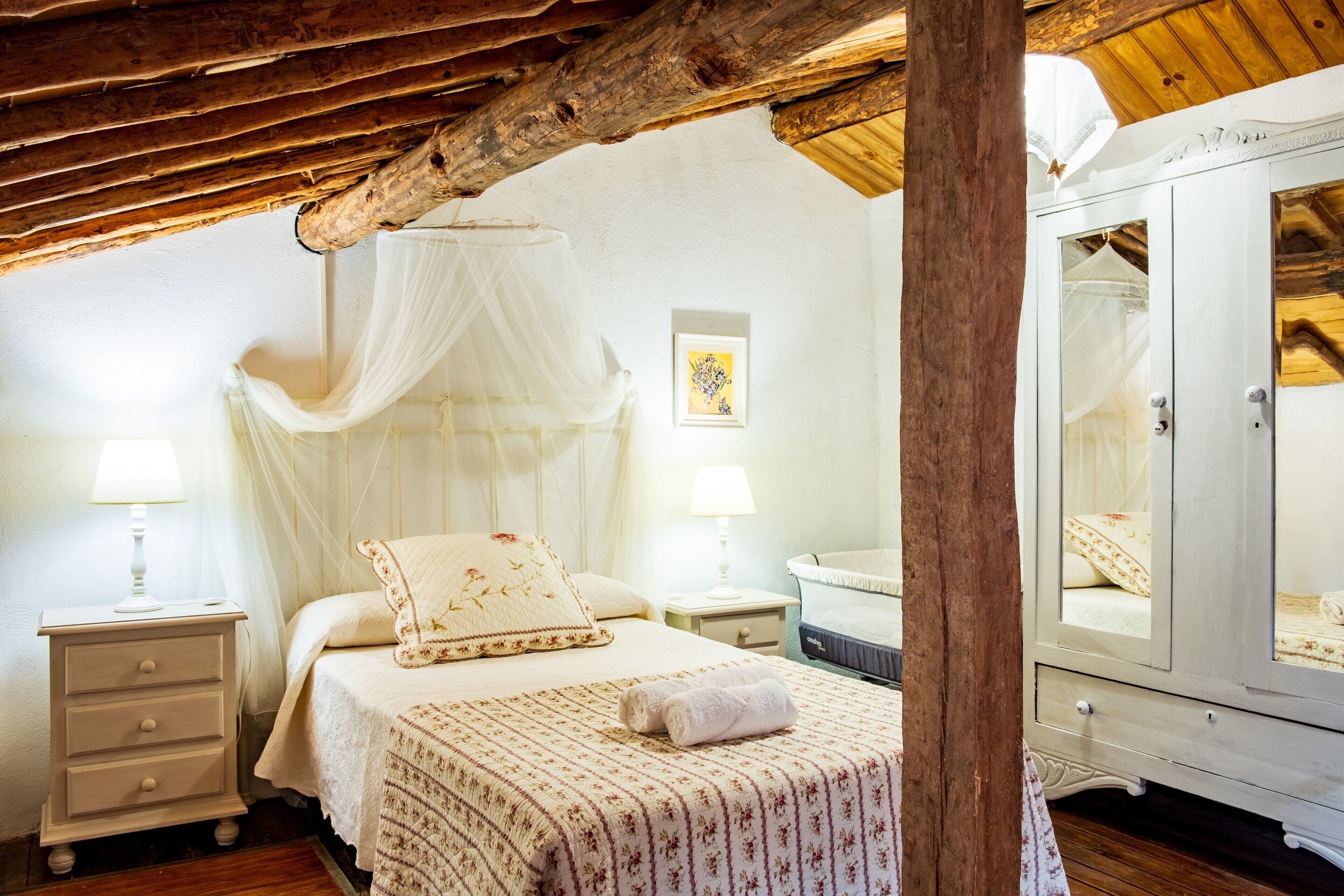 A bedroom with a canopy bed, a bedside table, a nightstand, a wardrobe, and a mirror.