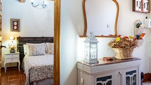 Un dormitorio con cama, mesitas de noche, espejo, candelabro y un mueble de pared con un cesto de flores secas.