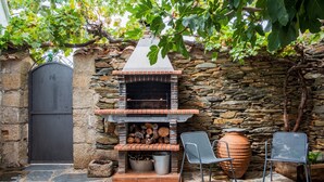Un muro de piedra con un horno de ladrillo, dos sillas de metal y una gran olla de barro.