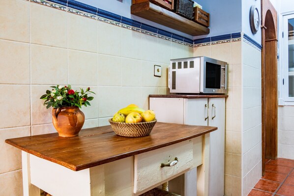 Une cuisine avec un plan de travail en bois, un four à micro-ondes, un placard et une plante en pot portant des fruits.