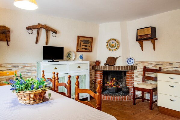 Un comedor con mesa, sillas, un cesto de flores, chimenea y adornos en la pared.