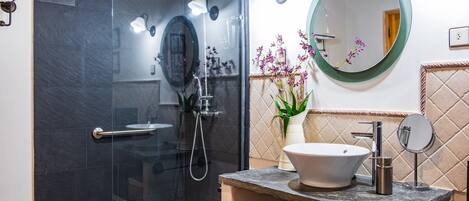 A modern bathroom with a glass-enclosed shower, a sink with a marble countertop, and a round mirror.