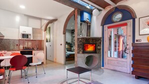 A modern kitchen with a microwave, dining table, and chairs. There is a fireplace with a visible fire, and a wooden cabinet.