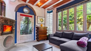 A living room with a fireplace, a sofa, a coffee table, and large windows with a view of trees.