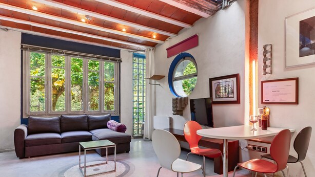 A modern living room with a sofa, chairs, a table, and large windows.