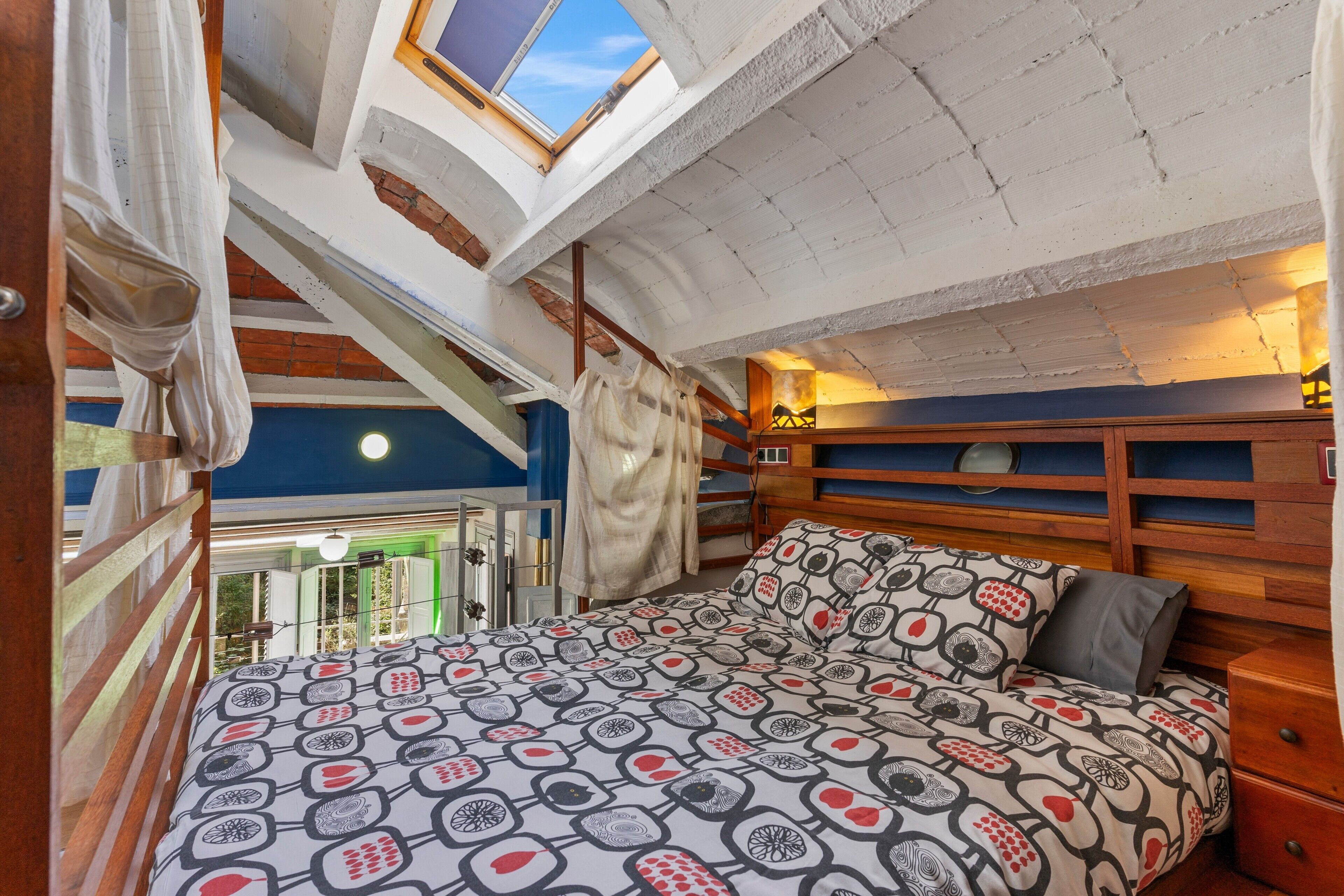 Een slaapkamer met een schuine plafond, een dakraam, een bed met een dessin en een houten hoofdeinde.