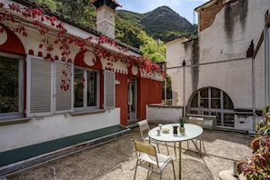 A courtyard with a round table and chairs, a small garden area, and a building with red and white walls. - Zentralclub Vatio Apartment with Mountain Views, Private Terrace and Wi-Fi (Belmonte De Miranda)