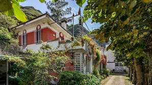 A building with a red and white facade, a garden with various plants, and a mountainous backdrop.