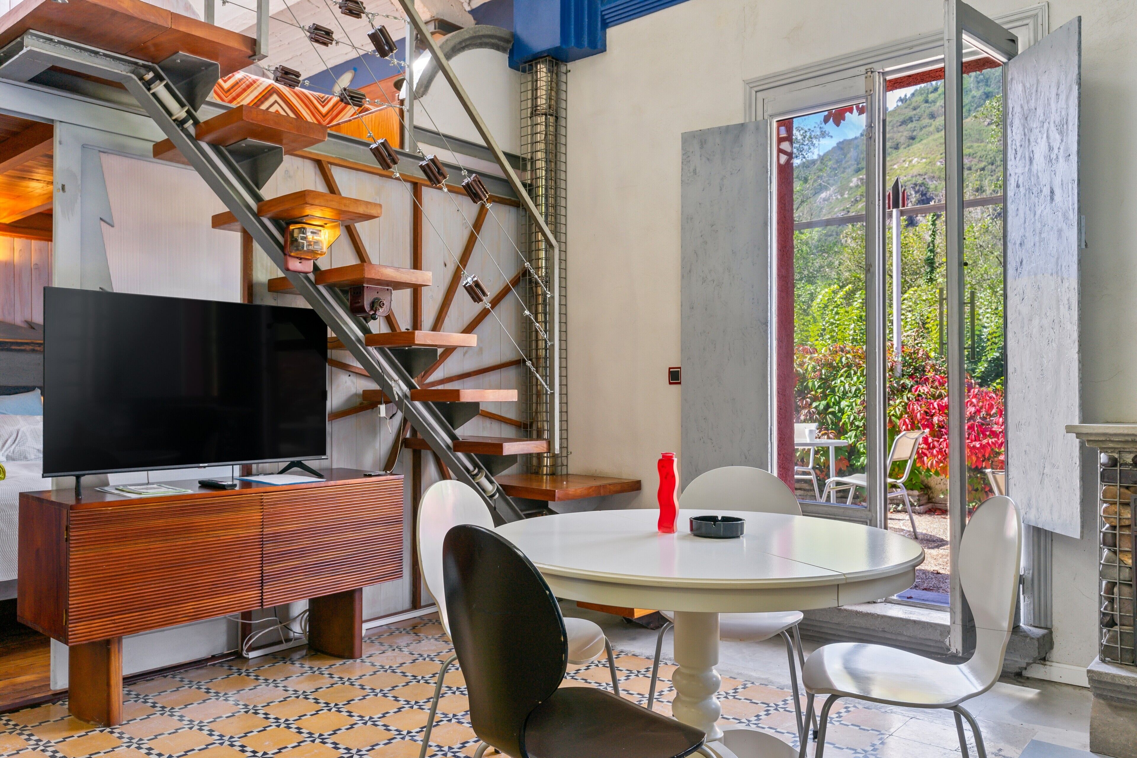 Un interior moderno con una escalera, un televisor de pantalla plana, una mesa de comedor y sillas.