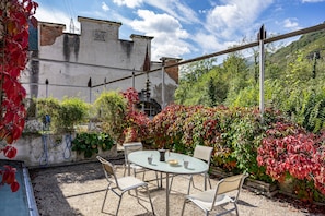 A patio with a table and chairs, surrounded by greenery and a building with a date plaque.