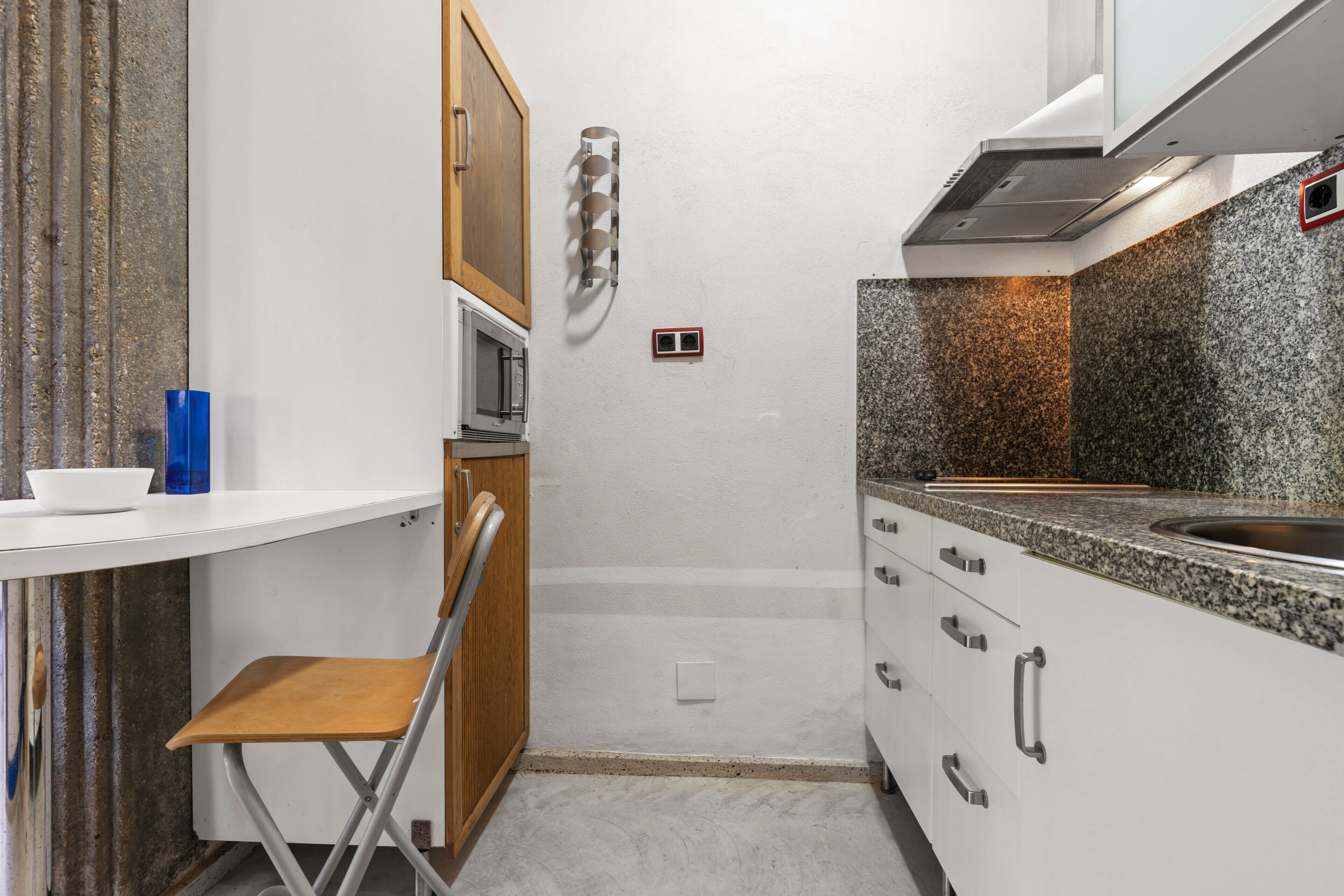 Une petite cuisine équipée d’un four à micro-ondes, d’un évier et d’une chaise en bois.
