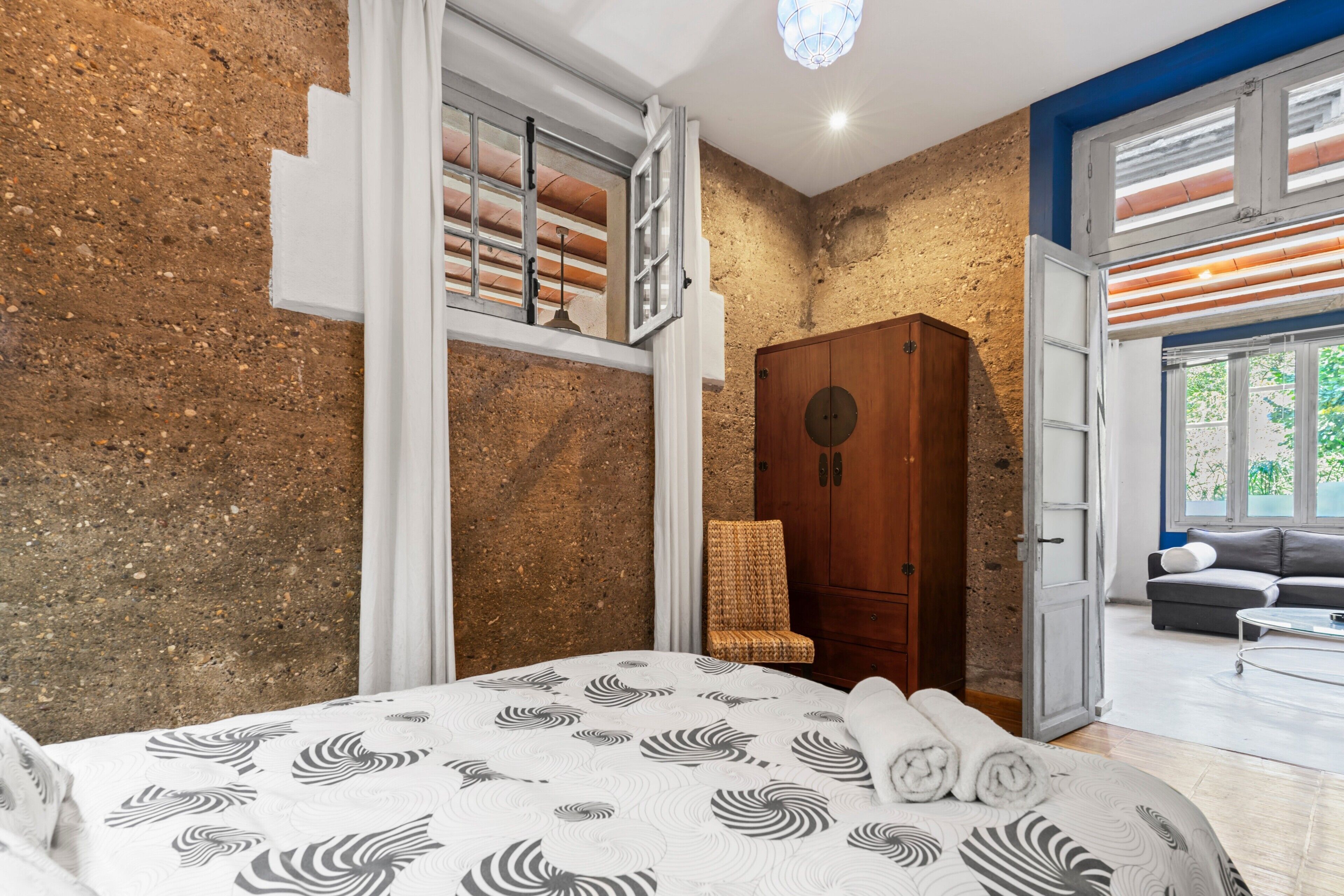 Un dormitorio con cama, un armario de madera, una silla de mimbre y vistas a un balcón.
