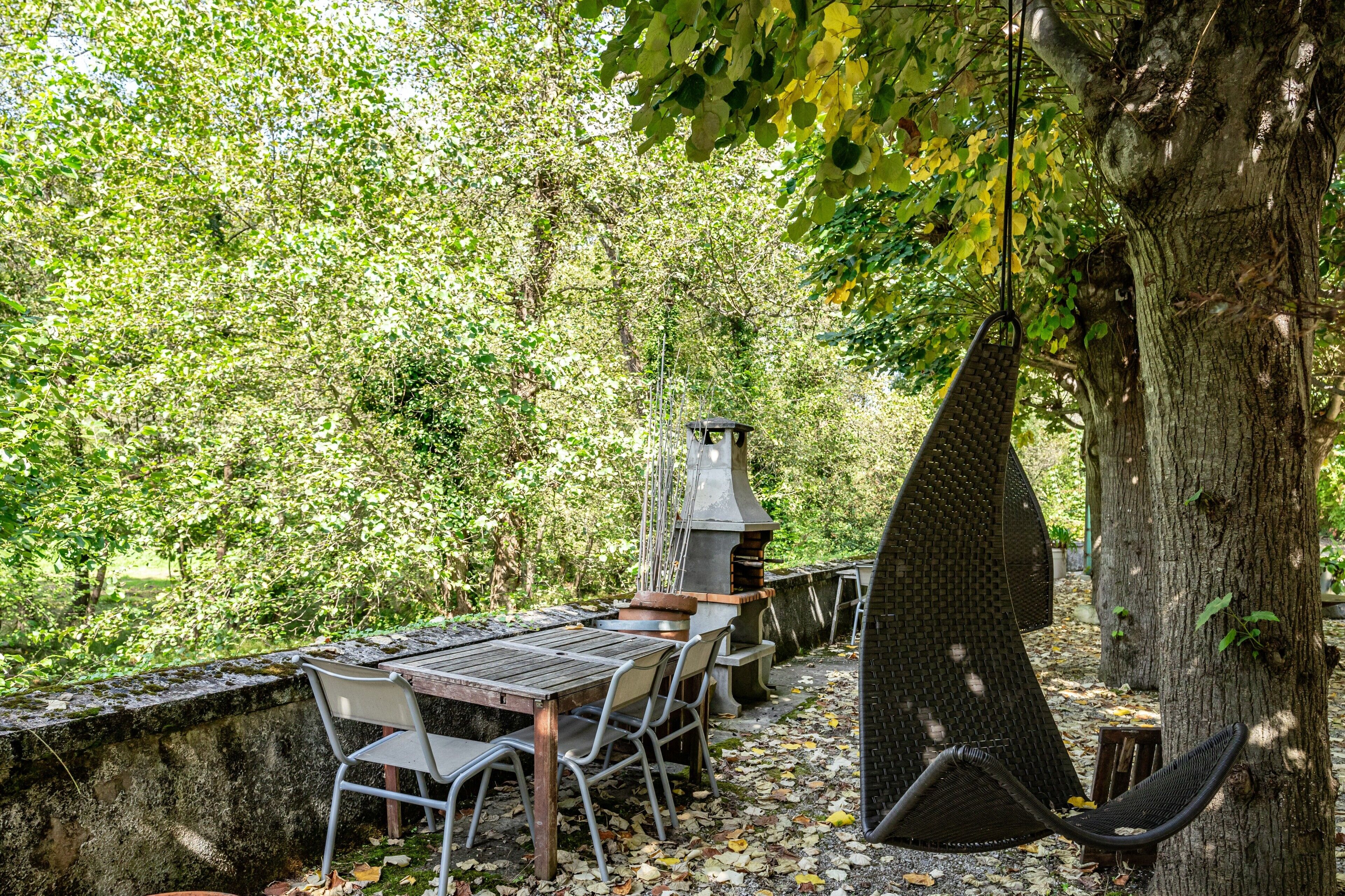 Un espacio de comedor al aire libre con una mesa y sillas, una hamaca colgante y una estructura de parrilla.