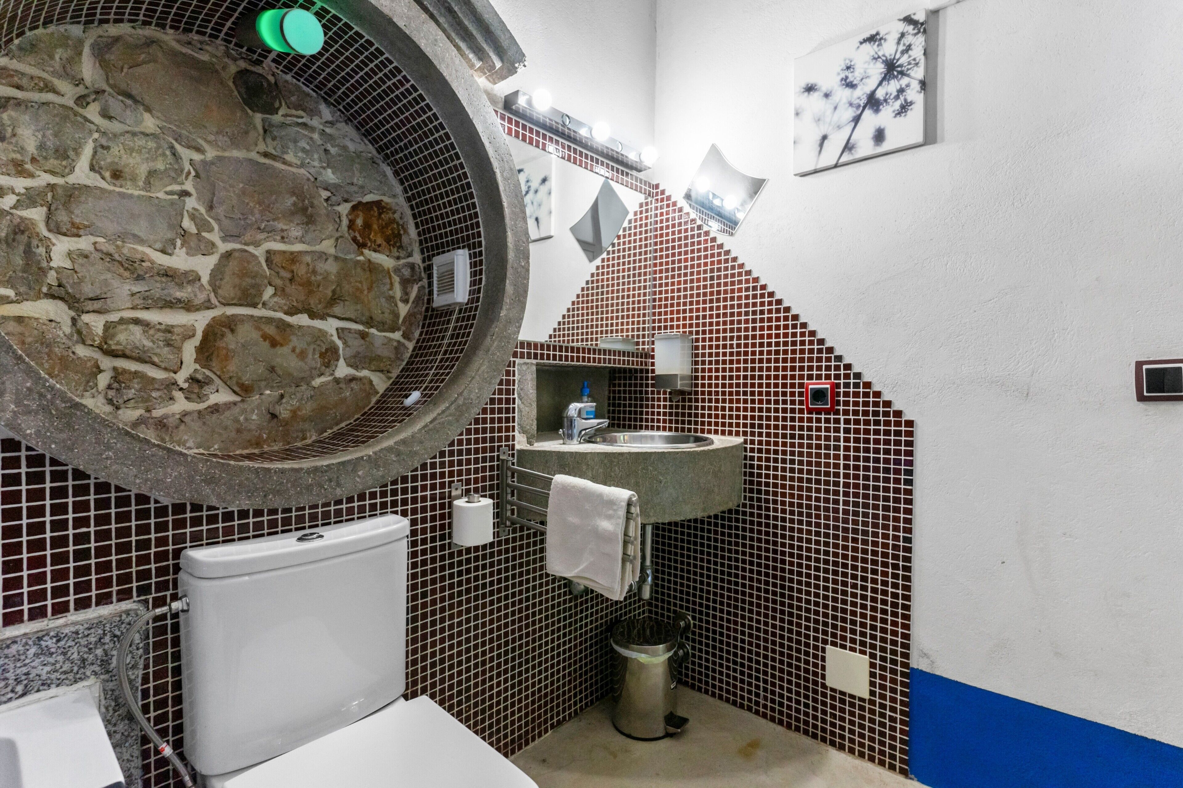 Un baño con un lavabo de piedra, un inodoro y un espejo con marco circular.