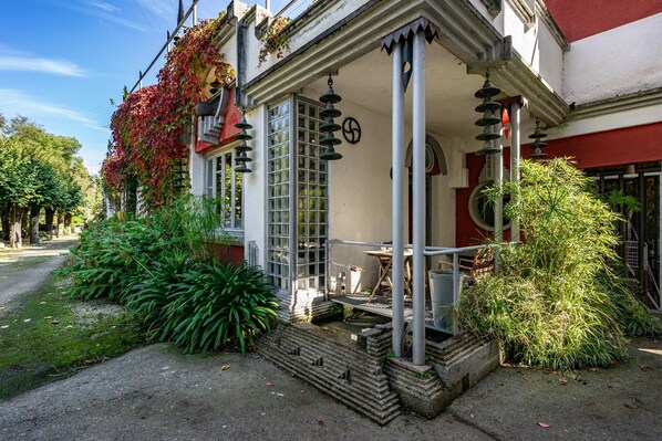 A building with a covered porch, a small water feature, and potted plants.