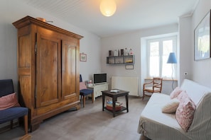 Un salon comprenant un meuble en bois, une télévision, un bureau, une chaise, un canapé et une fenêtre.