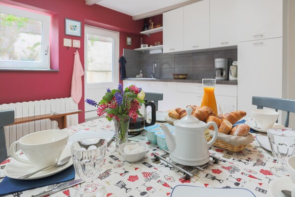 Une table de petit-déjeuner dressée avec une théière, des tasses, un bol de sucre, un vase de fleurs et des croissants.