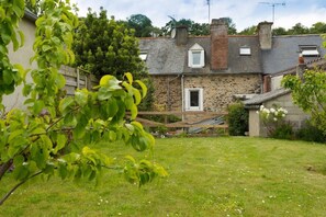 Une maison en pierre avec un petit jardin devant, une terrasse en bois et une antenne parabolique.