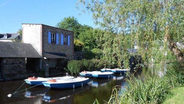 Un estrecho canal con barcos amarrados, un edificio de piedra y abundante vegetación.