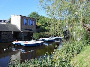 Un estrecho canal con barcos amarrados, un edificio de piedra y abundante vegetación.