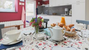 Mesa de desayuno dispuesta con tetera, tazas, un frutero con azúcar, un jarrón de flores y croissants.