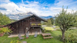 A wooden chalet with a deck, outdoor seating, and a mountain view. - Apartment 'La Charbonnière' with Mountain View, Private Garden and Wi-Fi (Cordon)