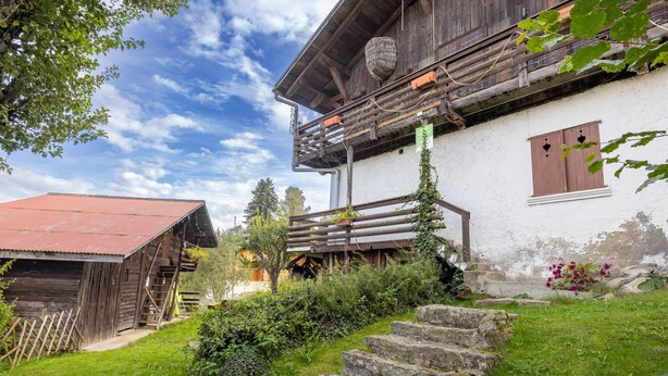 A rustic wooden building with a balcony, stone steps, and a red-roofed structure in the background. - Apartment 'La Charbonnière' with Mountain View, Private Garden and Wi-Fi (Cordon)