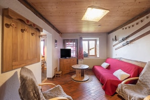 Ein gemütliches Zimmer mit Holzbalkendecke, einem roten Sofa, einem Fernseher und Skiern an der Wand.
