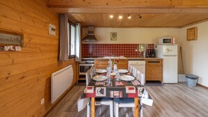 Een keuken met houten lambrisering, een eettafel voor vier personen, een magnetron en een koelkast.