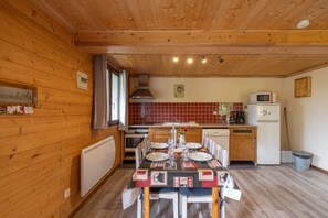A wooden-paneled kitchen with a dining table set for four, a microwave, and a refrigerator.