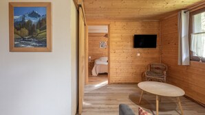 Een houten cabin interieur met een bed, een televisie, een eettafel en een schilderij van een berglandschap.