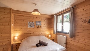 Een kamer met houten lambrisering, een bed, twee bedlampen, een radiator en een raam met gordijnen.