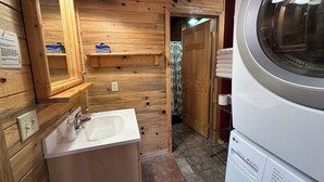 Un baño pequeño y acogedor, con paneles de madera, un lavabo, un espejo y una lavadora blanca.