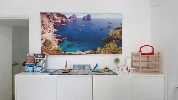 A room with a white cabinet, a painting of a coastal landscape, a small plant, and a red chair. - Apartment 'Penisola Apartments' with Shared Terrace, Wi-Fi and Air Conditioning (Vico Equense)